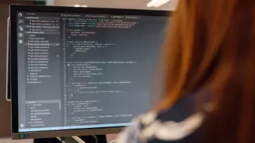 Persona al computer con codice sullo schermo.