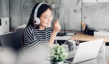 Persona con cuffie davanti a un laptop, sorridente.